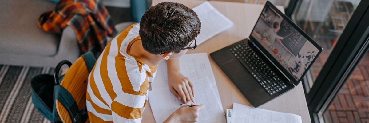 Boy participating in online education training class with teacher using laptop at home